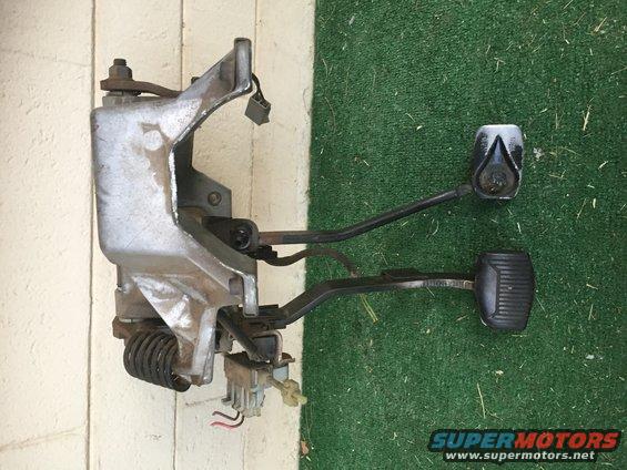 Metal brake and clutch pedal assembly with black rubber pads, mounted on a bracket with springs and wiring