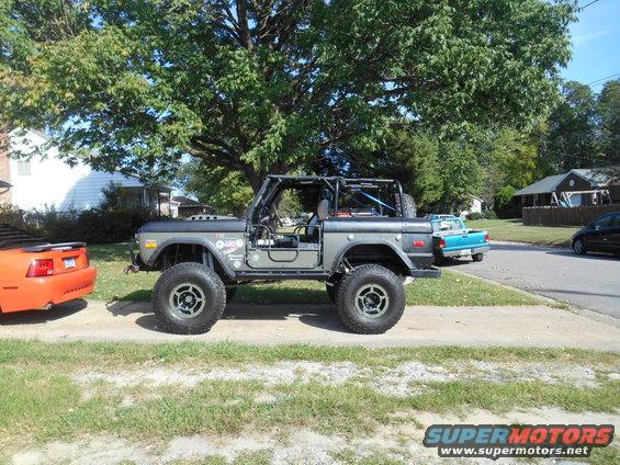 Gray 1972 Ford Bronco with roll cage and off-road tires parked next to an orange Mustang