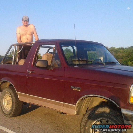 Maroon 1996 Ford Bronco, driver's side, with a man standing in the open roof, side trim visible