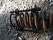 1986 Ford Bronco - A rusty coil spring and a spring compressor tool lie on a gravel surface.