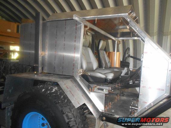 Custom vehicle build with seats and steering wheel visible, unfinished metal body panels