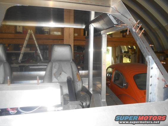 Orange VW Beetle parked inside a workshop, viewed from the interior of a partially built structure