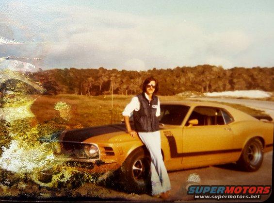 Yellow 1970 Boss 302 Mustang with black stripes, man leaning on hood