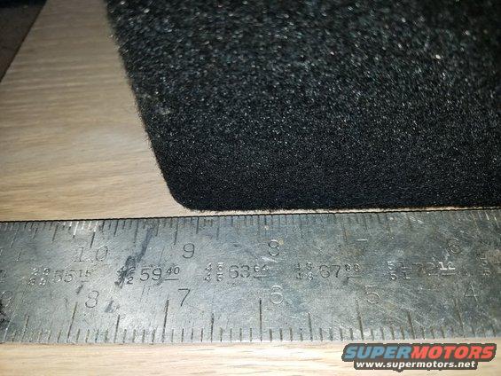 Black carpeted object measured by a ruler showing inches and fractions