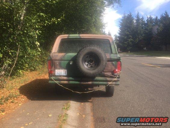 Rear view of a 1978 Ford Bronco in camouflage paint with a spare tire mounted on the tailgate