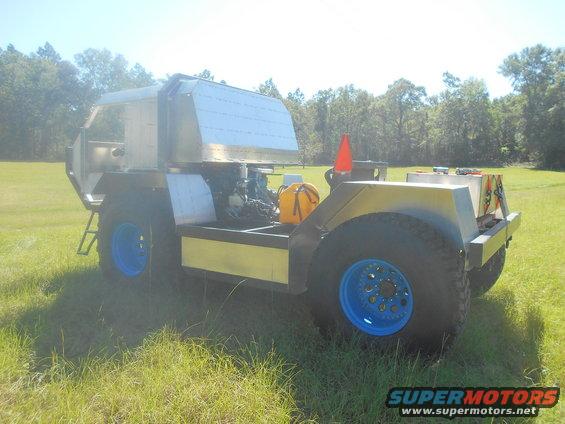 Custom off-road vehicle with large tires and blue rims, parked in a grassy field