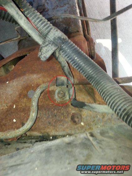 Close-up of rusted metal frame with a wiring harness secured by a bolt, highlighted by a red circle
