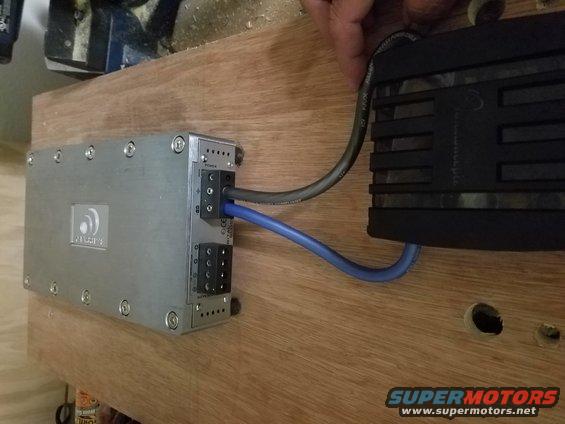 Car amplifier connected to a power supply with blue and gray wires. Some text is visible on the amplifier