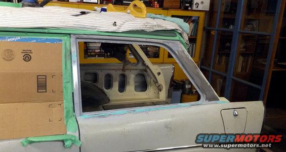 Car door frame with tape and primer, showing interior paneling and window opening. Boxes stacked on the left