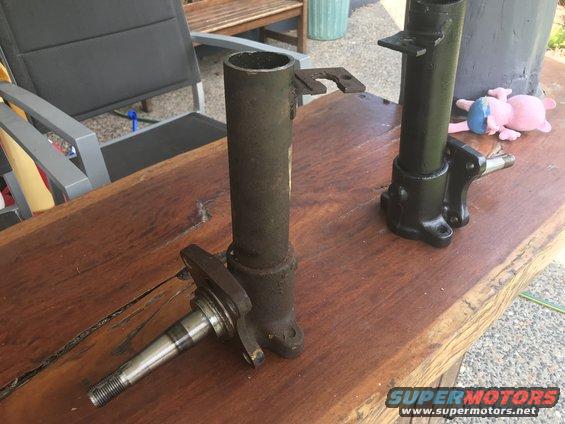 Two automotive steering knuckles on a wooden table. One is rusty, the other is painted black
