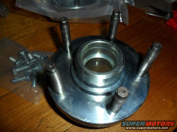 Wheel hub with five studs and a central bearing race, next to a bag of bolts