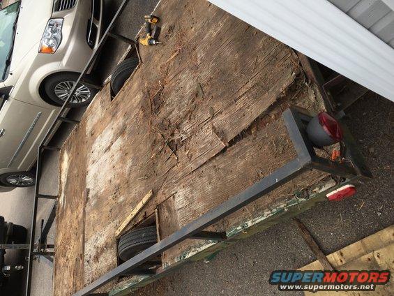 trailer with worn wood deck, spare tire visible, and a minivan parked next to it