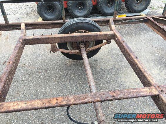 rusted trailer frame with one wheel and leaf spring visible, other tires in background