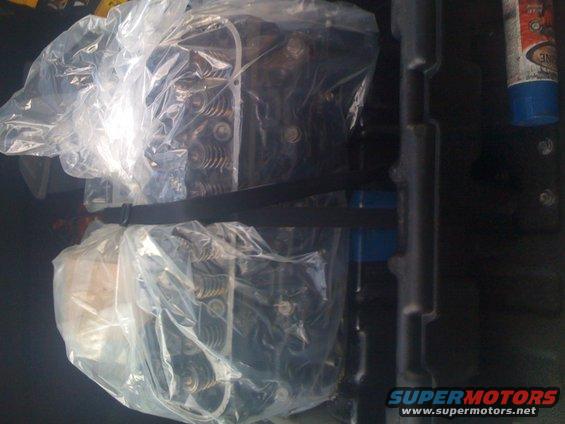 Engine cylinder heads covered in plastic wrap, secured with a black strap