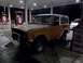 1969 Ford Bronco - An orange SUV is parked at a gas station at night, viewed from the front three-quarter angle.