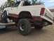 1984 Ford Bronco - White and red Ford Bronco loaded onto a trailer, showing its lifted suspension and large off-road tires.