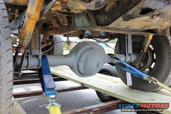 Undercarriage view of a vehicle's rear differential and suspension, secured with straps on a trailer