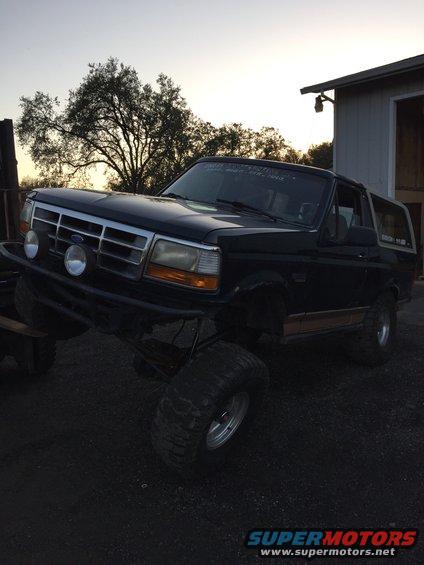 Black Ford Bronco with lifted suspension and aftermarket bumper. Visible woodgrain trim on the side