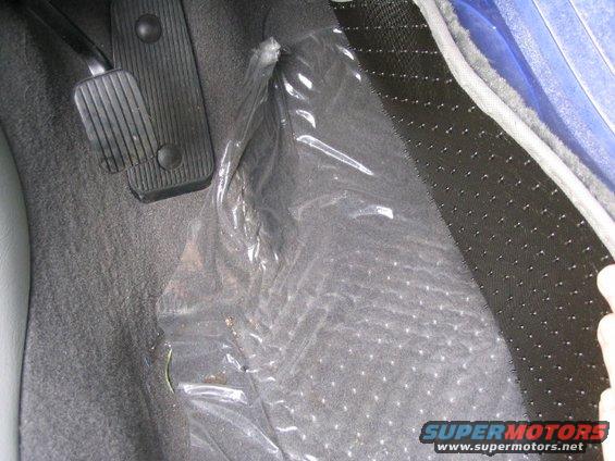 Car floor with plastic sheeting over carpet, showing brake and gas pedals