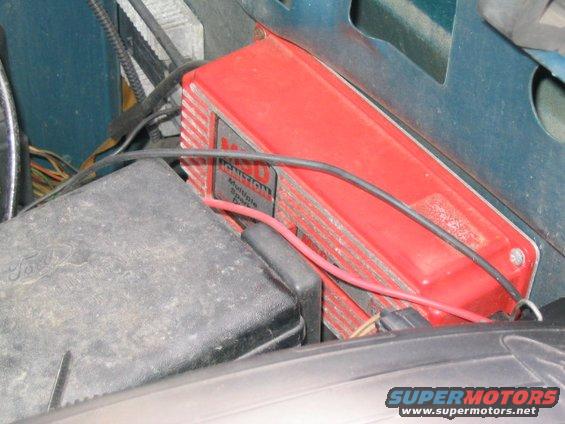 Red ignition control module with wires connected. A black box with 'Ford' visible is to the left
