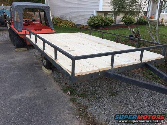 Red amphibious vehicle with a black canopy is parked on a trailer with a new wooden deck