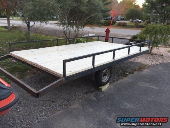 Side view of a wooden-decked utility trailer with metal railings