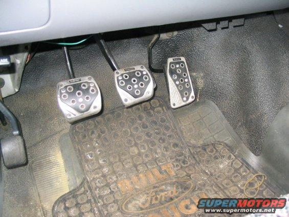 Three aftermarket pedals and a dirty Ford-branded floor mat in a vehicle interior