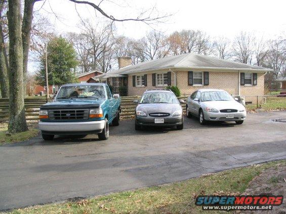 Blue Ford pickup truck, gray sedan, and silver sedan parked in front of a brick house