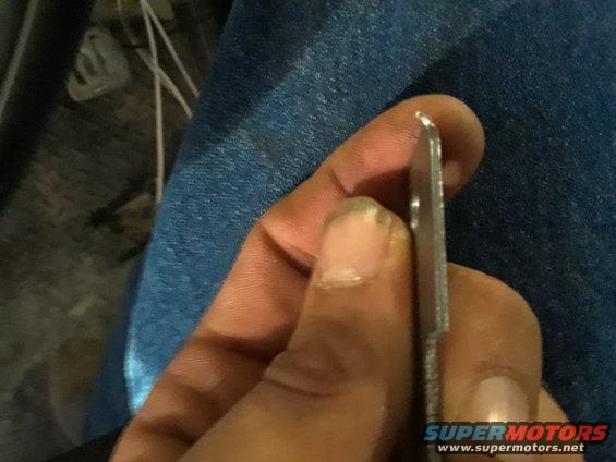Close-up of a metal part held by a hand, with a Supermotors.net watermark at the bottom