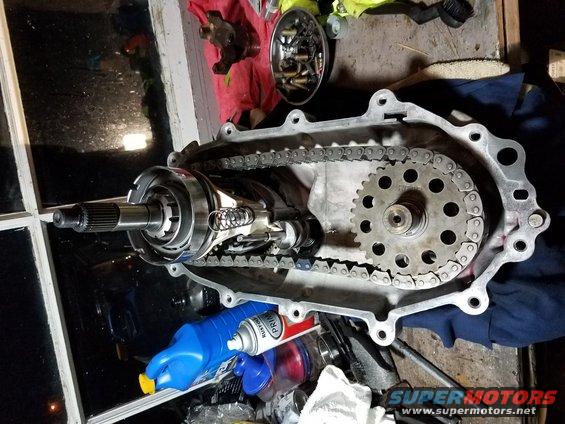 transfer case with chain and gears exposed, some tools and fluids nearby