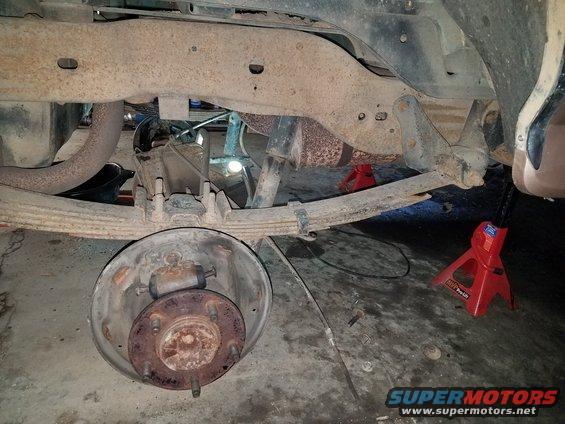 Rear axle assembly with leaf springs, shock absorber, and brake drum removed. Vehicle is supported by jack stands