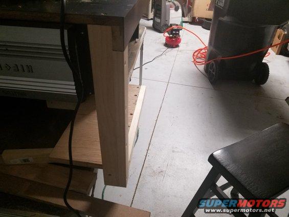 Workbench with wooden legs, air compressor, and trash can in a garage