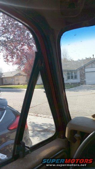 Interior view of a vehicle's door frame and window, showing part of a steering wheel and another car outside