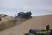 2000 Ford F-450 - A blue pickup truck navigates a sandy incline, kicking up dust. Another vehicle is partially visible in the foreground.