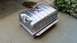1985 Ford Bronco - A new metal gas tank, likely for a classic vehicle, sits on a concrete surface next to some greenery.