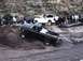 2000 Ford F-450 - A group of friends and their trucks gather for off-road fun, with one truck navigating a steep incline near water.