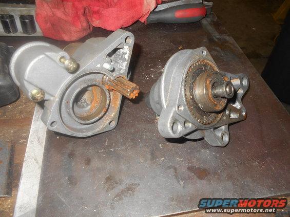 Two disassembled starter motors on a workbench, showing rusty gears and shafts