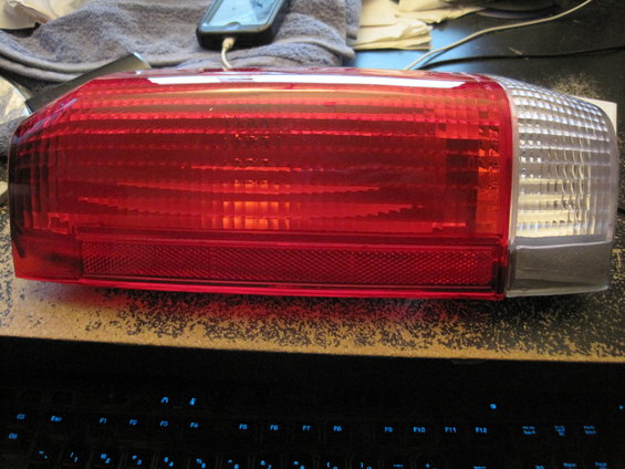 Red taillight assembly with clear corner section, resting on a surface above a keyboard