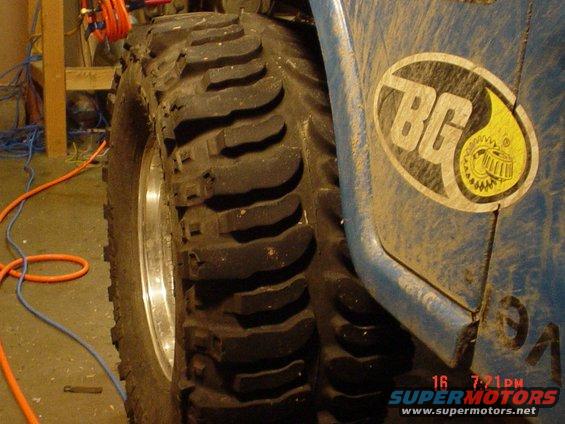 Close-up of a large off-road tire and blue fender with a BG logo. Watermark shows 'SUPERMOTORS'