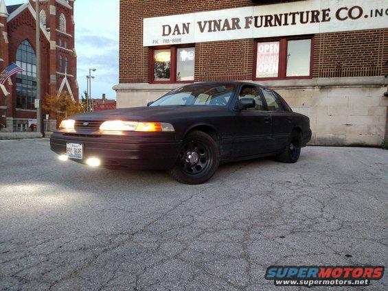 Black sedan parked in front of Dan Vinar Furniture Co. with its headlights on