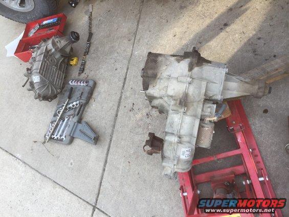 Two transfer cases, one on a red jack, with a toolbox and wrenches on concrete