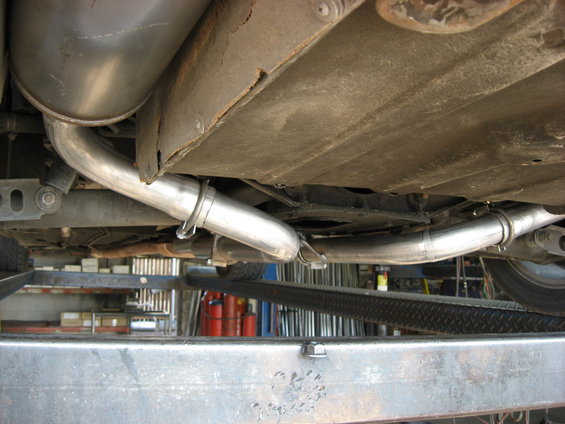 Underside view of a car's exhaust pipes and muffler, showing new stainless steel piping
