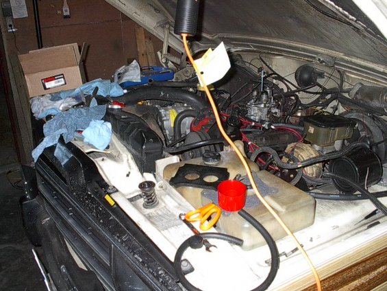 Engine bay of a Jeep with tools and parts scattered around. An orange extension cord runs through the scene