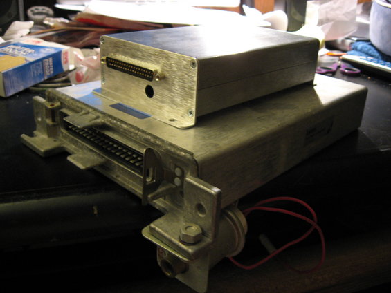 Two stacked metal electronic control units with multiple connectors and red wires