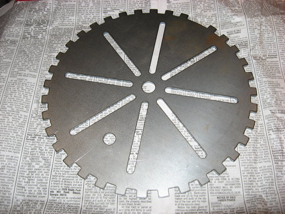 Metal gear with 12 teeth and 8 radial cutouts, resting on newspaper pages