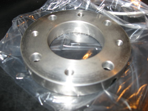 Metal flange with eight bolt holes, still in plastic packaging
