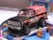 1979 Ford Bronco - A black toy truck with a red top and 'MUDSTER' graphics sits on a display ramp.