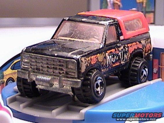 Black toy truck with orange top and "Monster" graphics, seen from a 3/4 front angle
