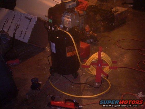 Black air compressor with yellow hose and red tool