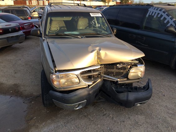 Gold SUV with heavily damaged front end, parked in a lot with other vehicles
